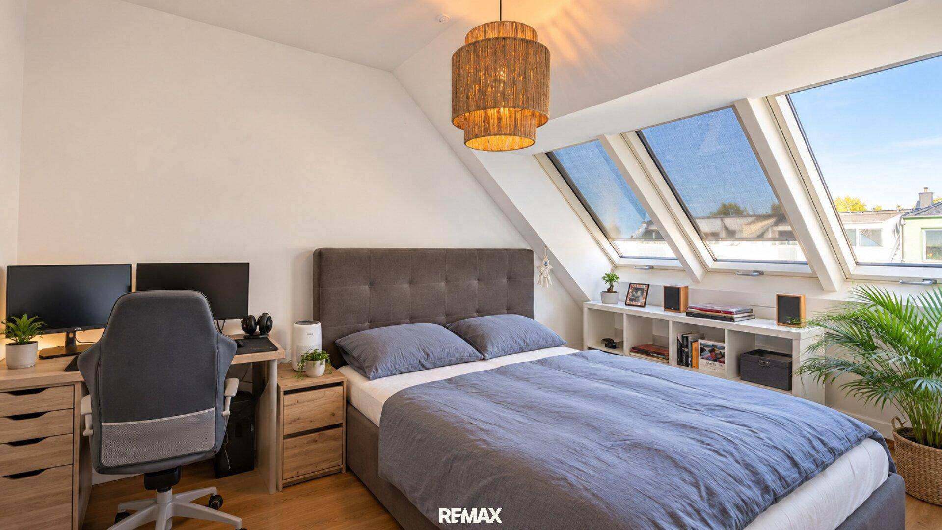 Schlafzimmer mit Arbeitsbereich, Holzboden und schrägen Wänden, hell durch große Dachfenster.