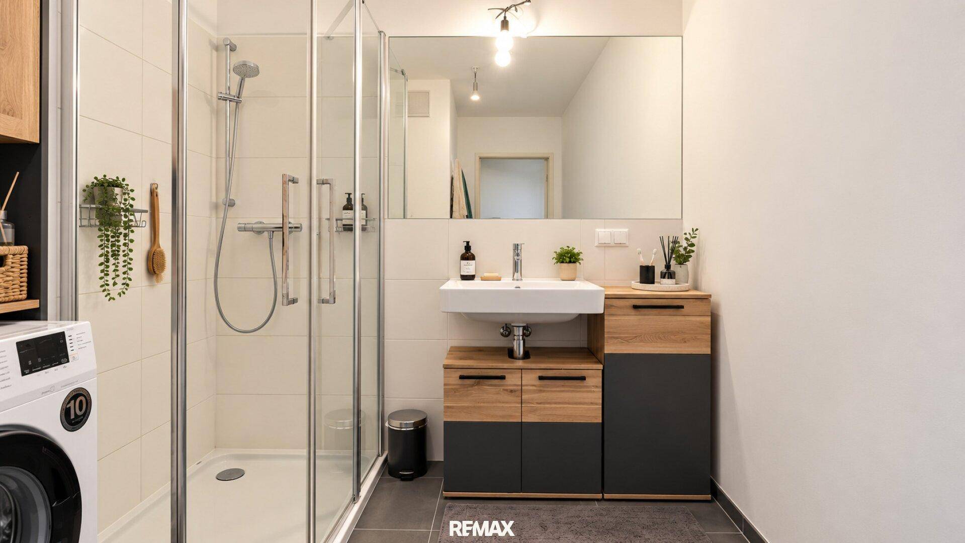 Modernes Badezimmer mit Dusche, Waschbecken und Waschmaschine, ausgestattet mit dunklen Fliesen.