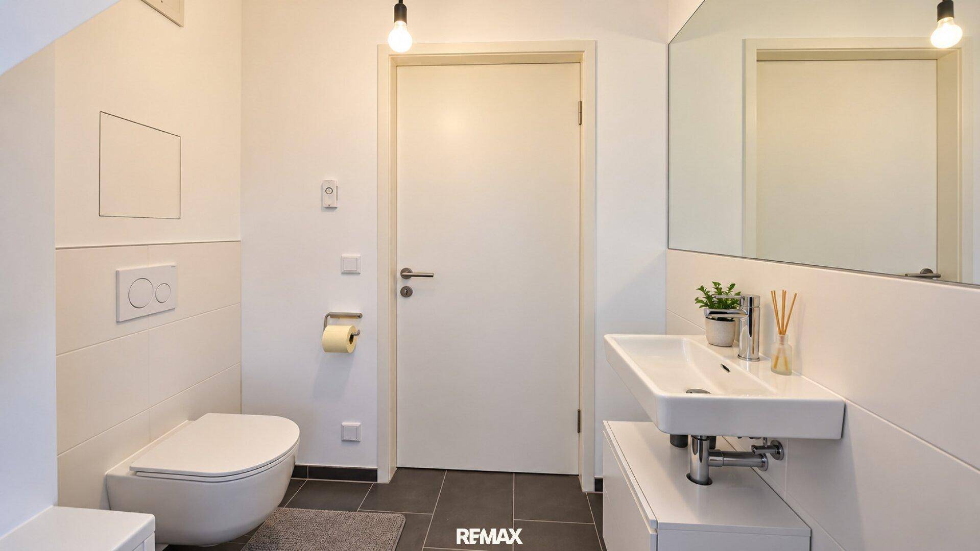 Separates WC mit wandhängender Toilette und modernem Waschbecken, hell gefliest.