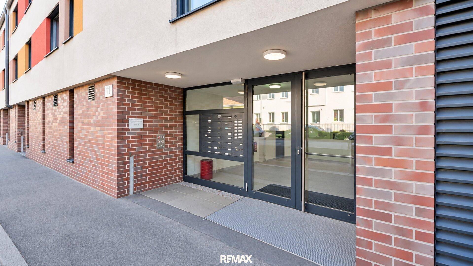 Moderner Gebäudeeingang mit Glasfront und Ziegelmauerwerk, barrierefrei zugänglich.