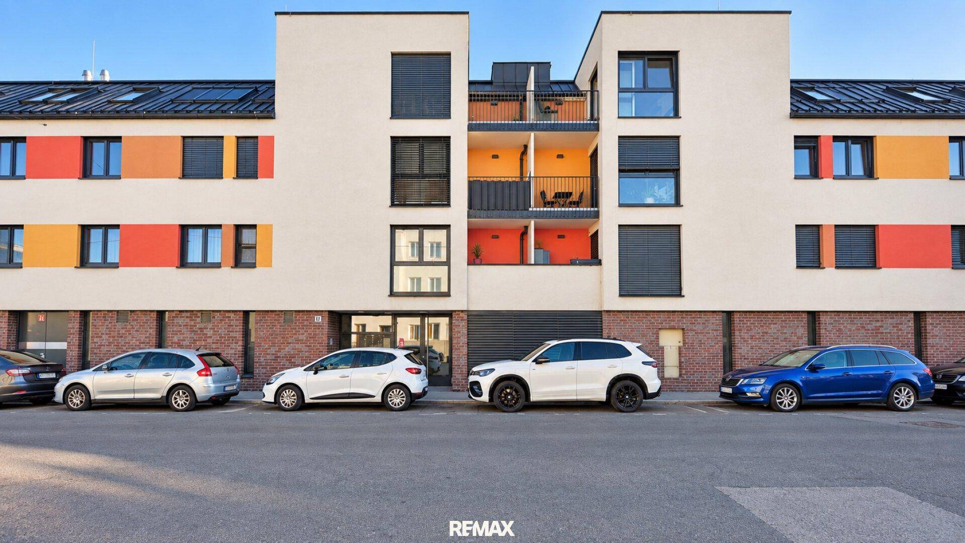 Moderne Wohnanlage mit farbigen Akzenten an der Fassade und Parkplätzen davor.