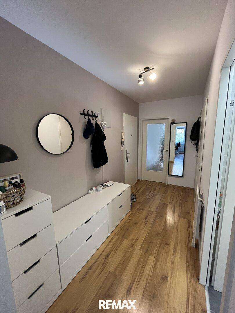 Heller Flur mit praktischen weißen Kommoden, Spiegel und Garderobe.