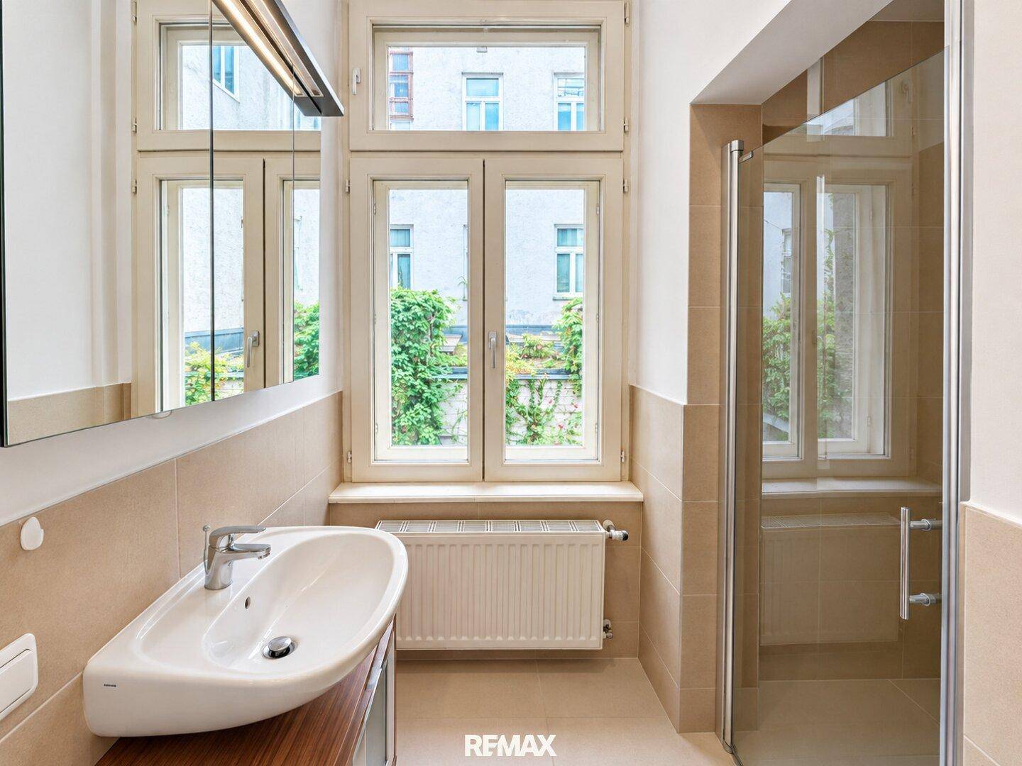 Modernes Badezimmer mit Dusche, Einzelwaschbecken und Fenster mit Blick auf eine grüne Wand.