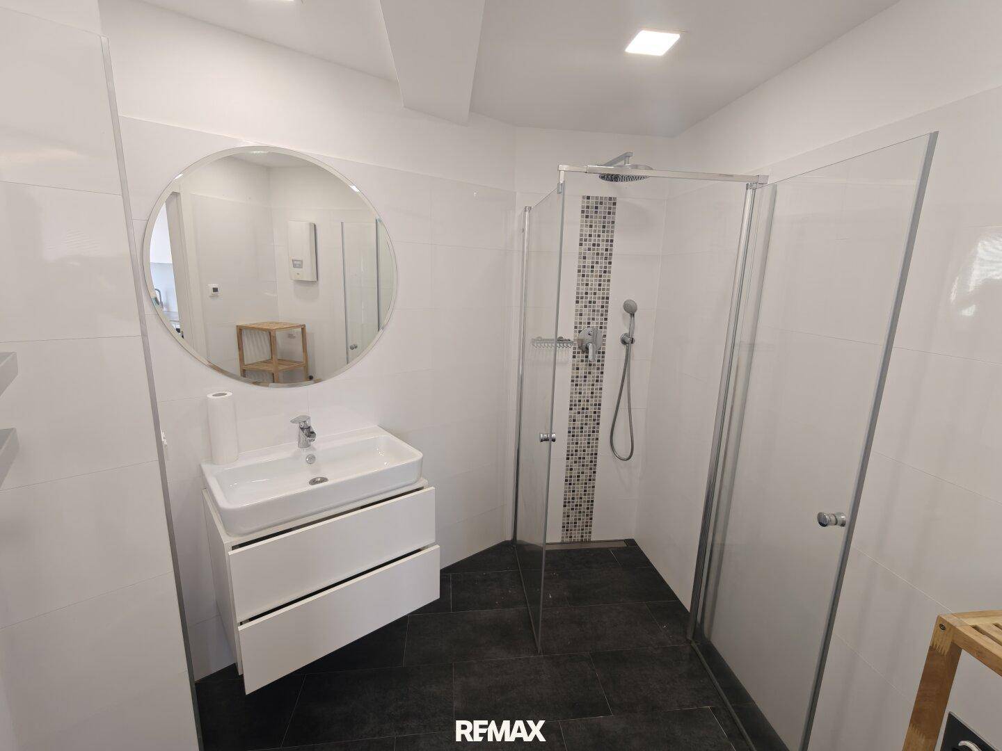 Modernes Badezimmer mit Duschkabine, Waschbecken und dunklen Bodenfliesen.
