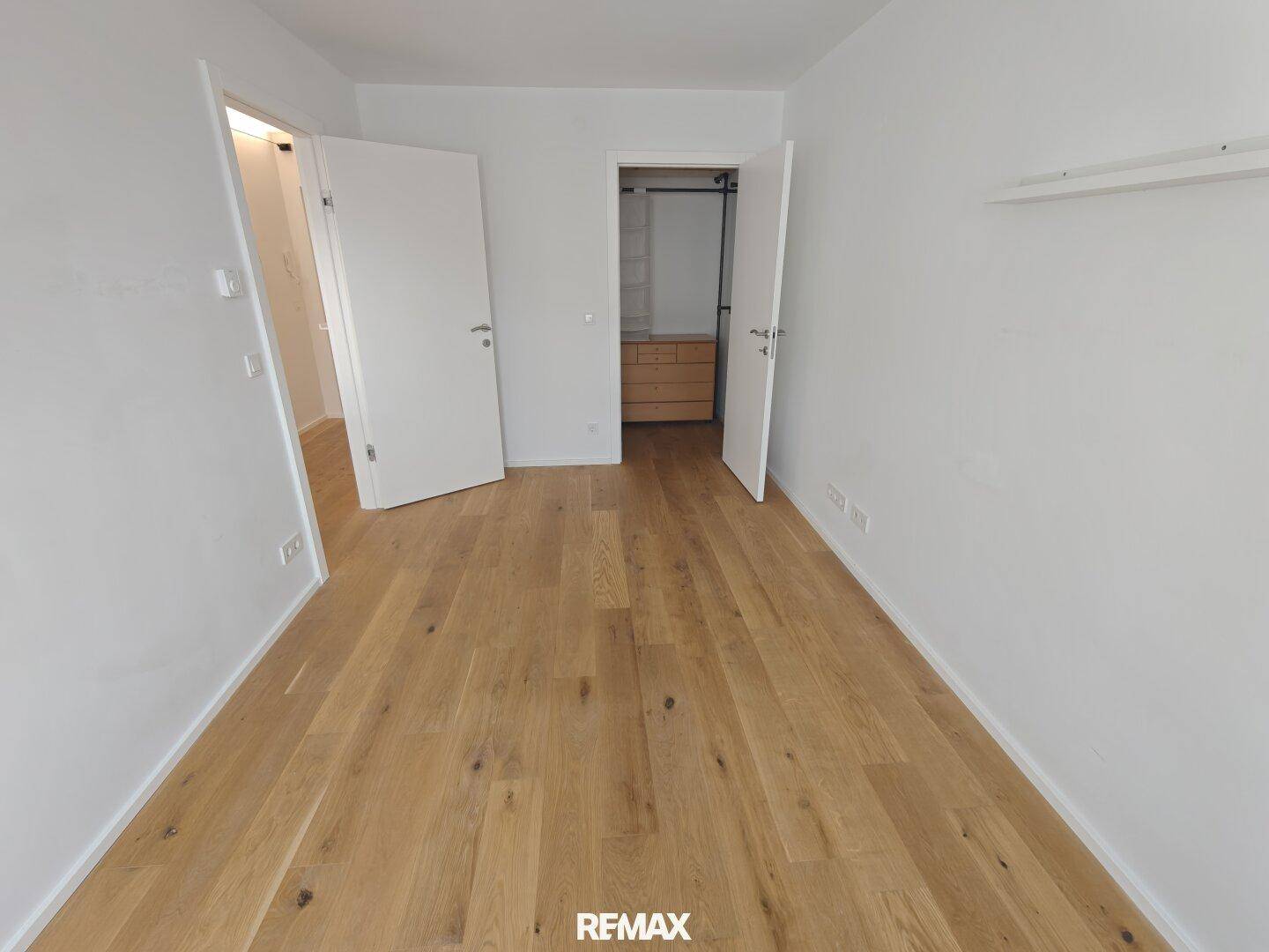 Heller Raum mit Holzboden und offenen Türen, die zu weiteren Zimmern führen.