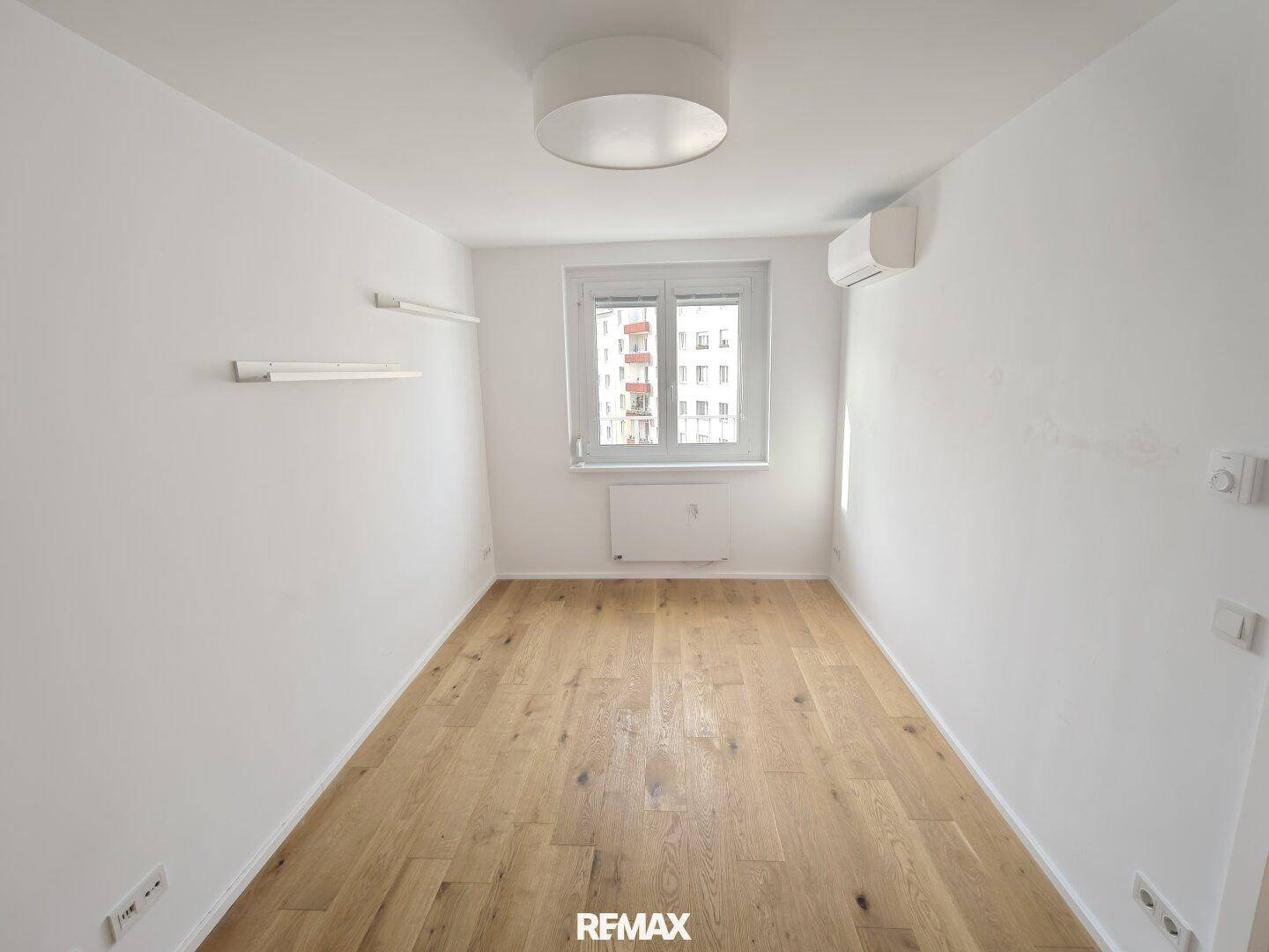 Leeres Zimmer mit Holzboden, Fenster und installierter Klimaanlage.