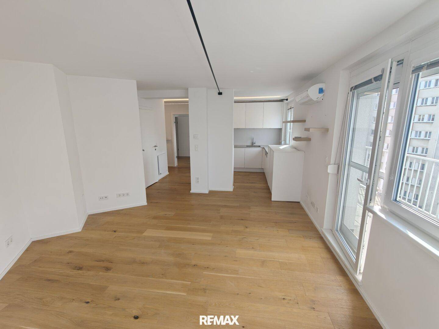 Offener Wohnbereich mit Holzboden, integrierter Küche und Zugang zum Balkon.