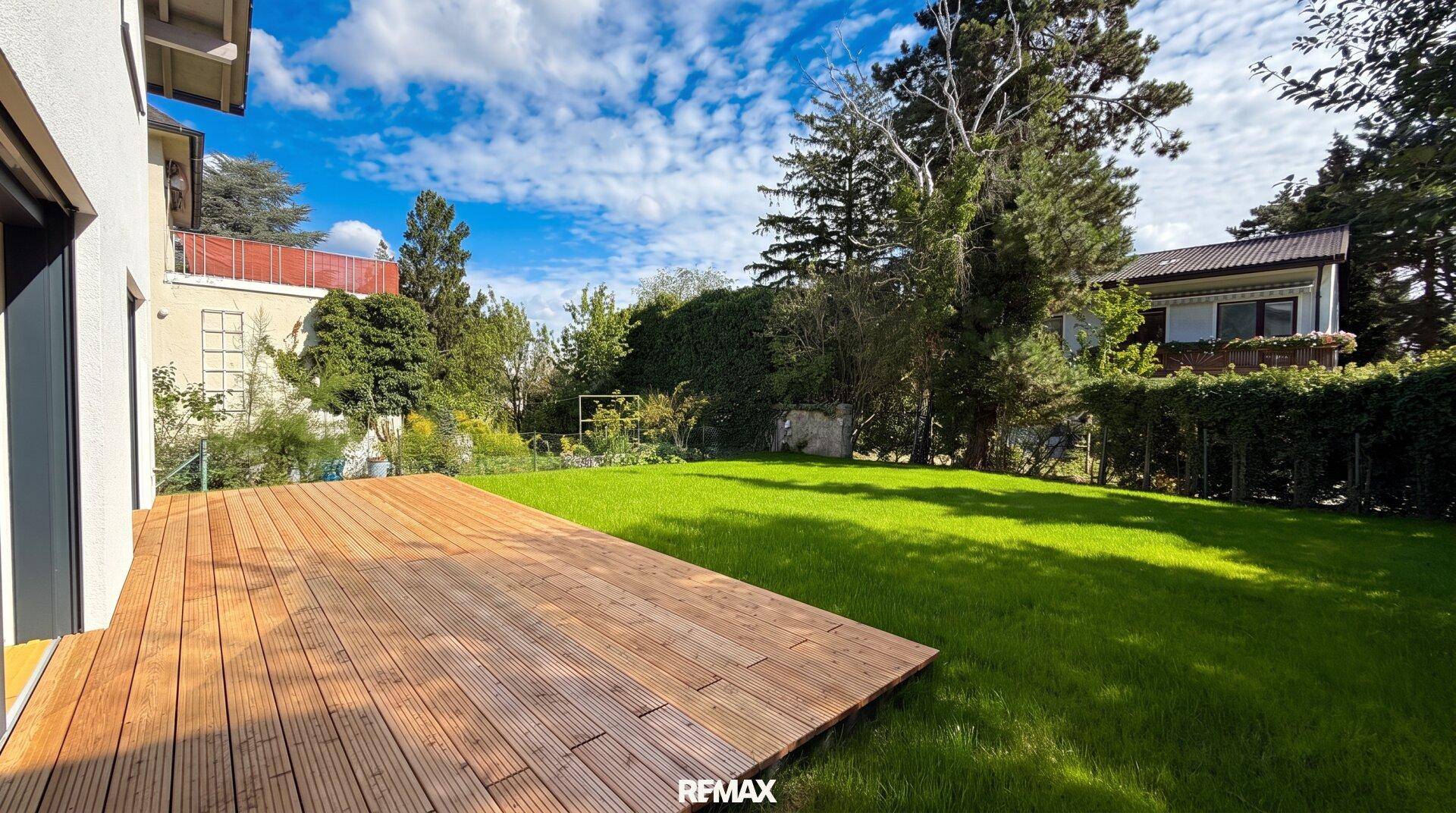 Weitläufiger Garten mit Holzterrasse und viel Grün, ideal für Entspannung im Freien.