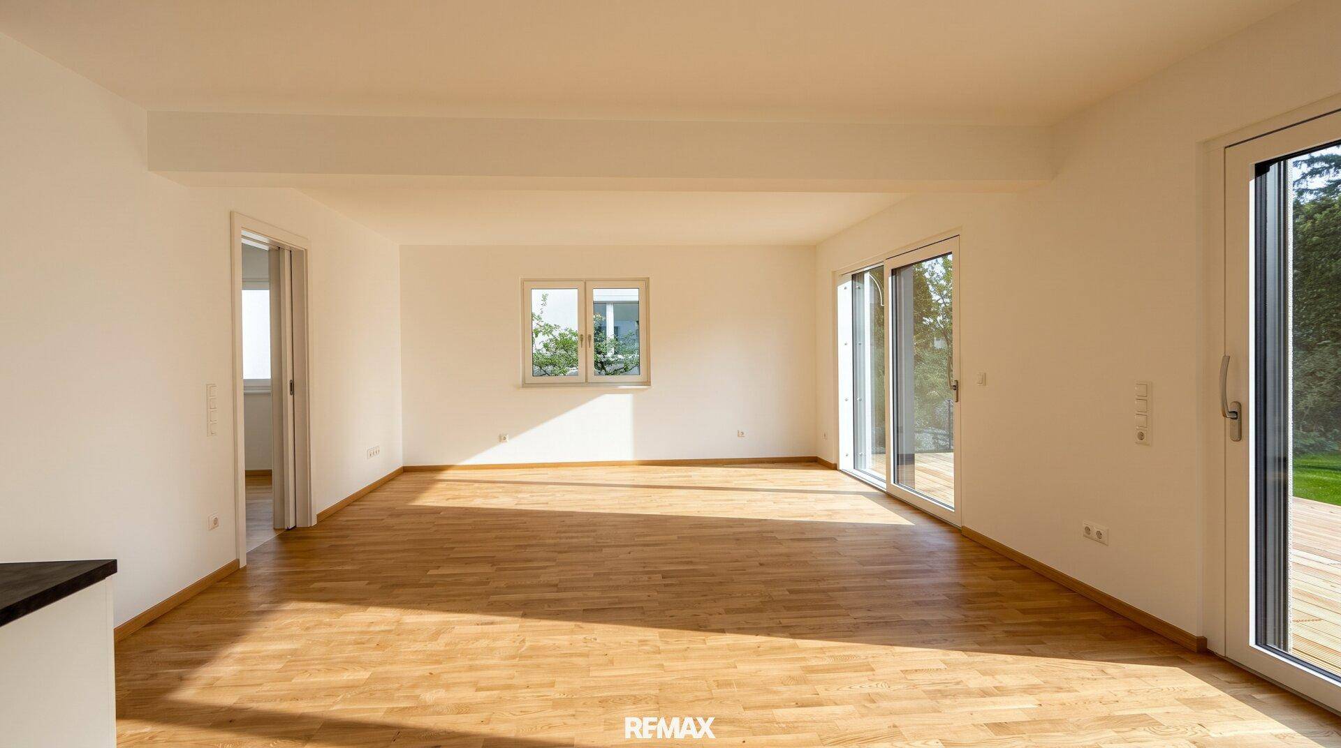 Geräumiges Wohnzimmer mit Holzboden und viel Tageslicht durch große Fenster.
