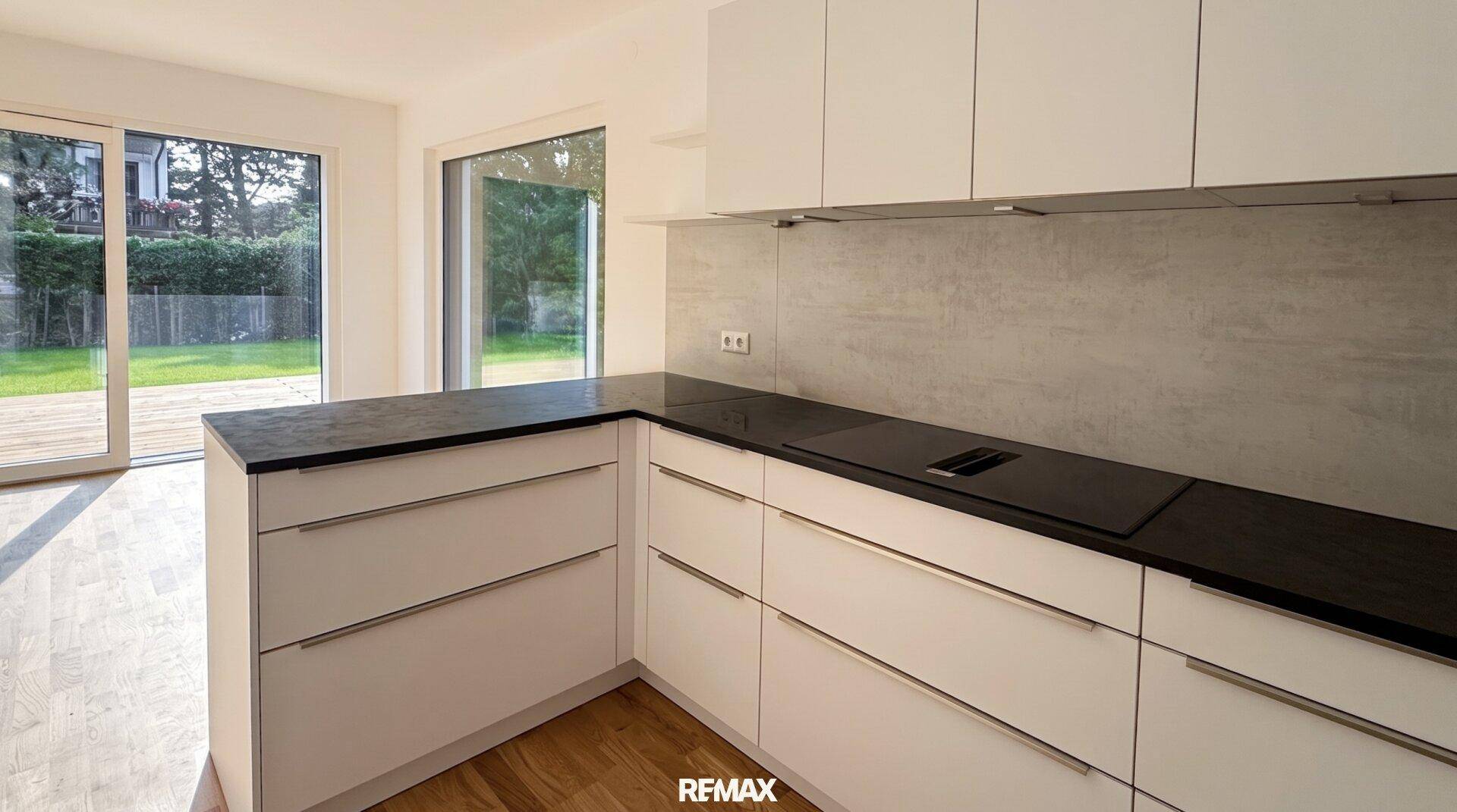 Helle Küche mit modernen weißen Fronten, dunkler Arbeitsplatte und Zugang zur Terrasse.