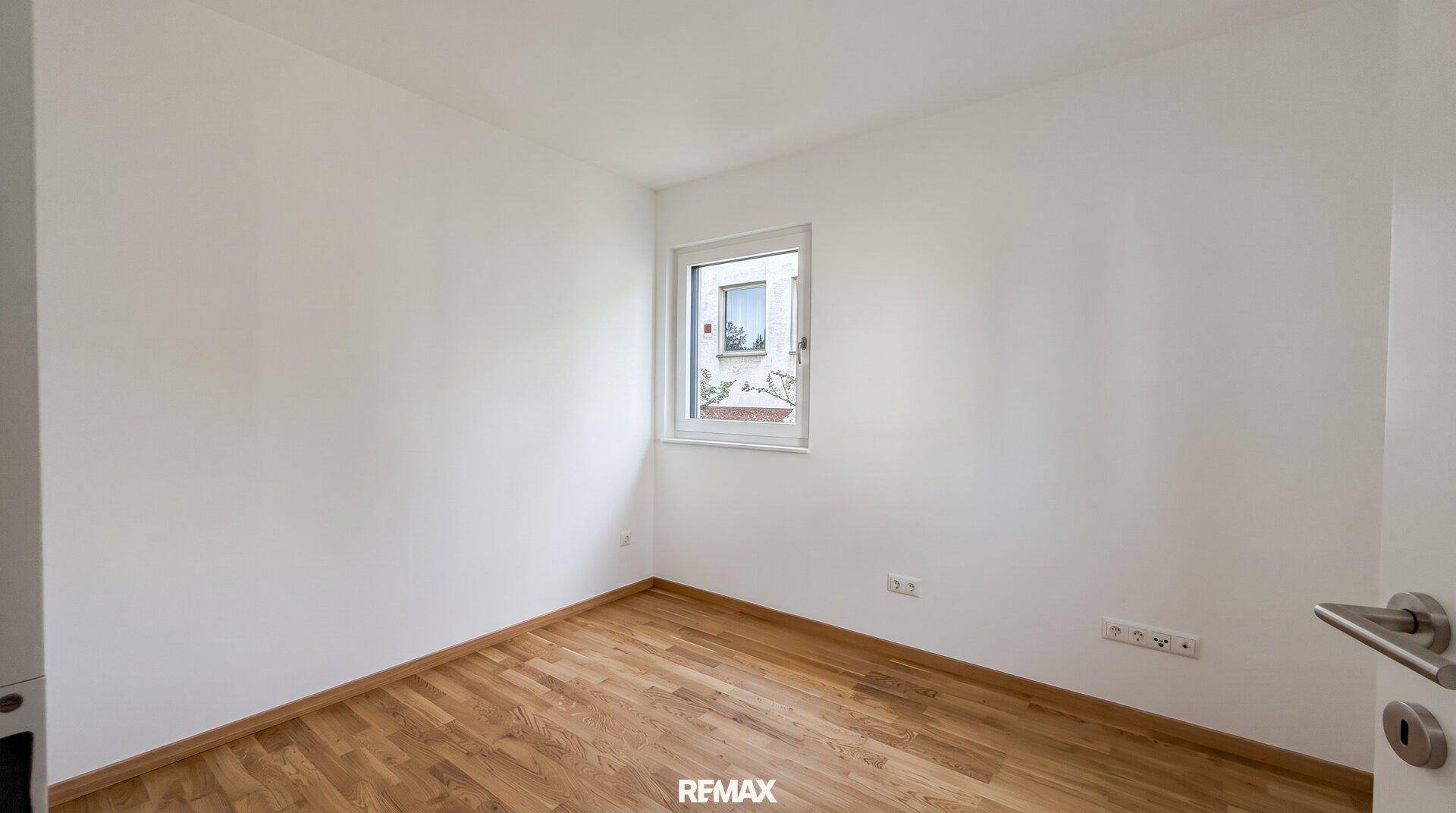 Helles Schlafzimmer mit Holzboden und Fenster mit Blick ins Grüne.