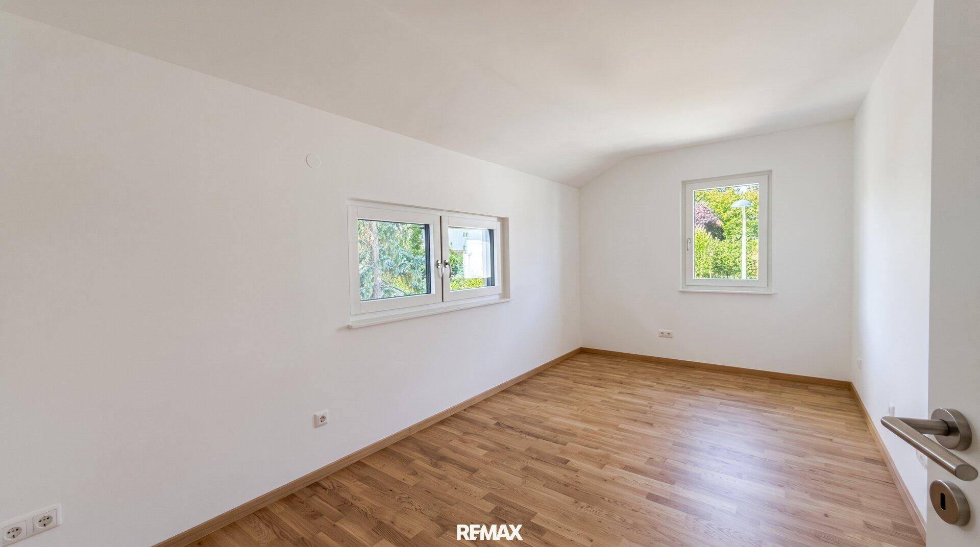 Geräumiges Schlafzimmer mit Holzboden und zwei Fenstern für viel Tageslicht.