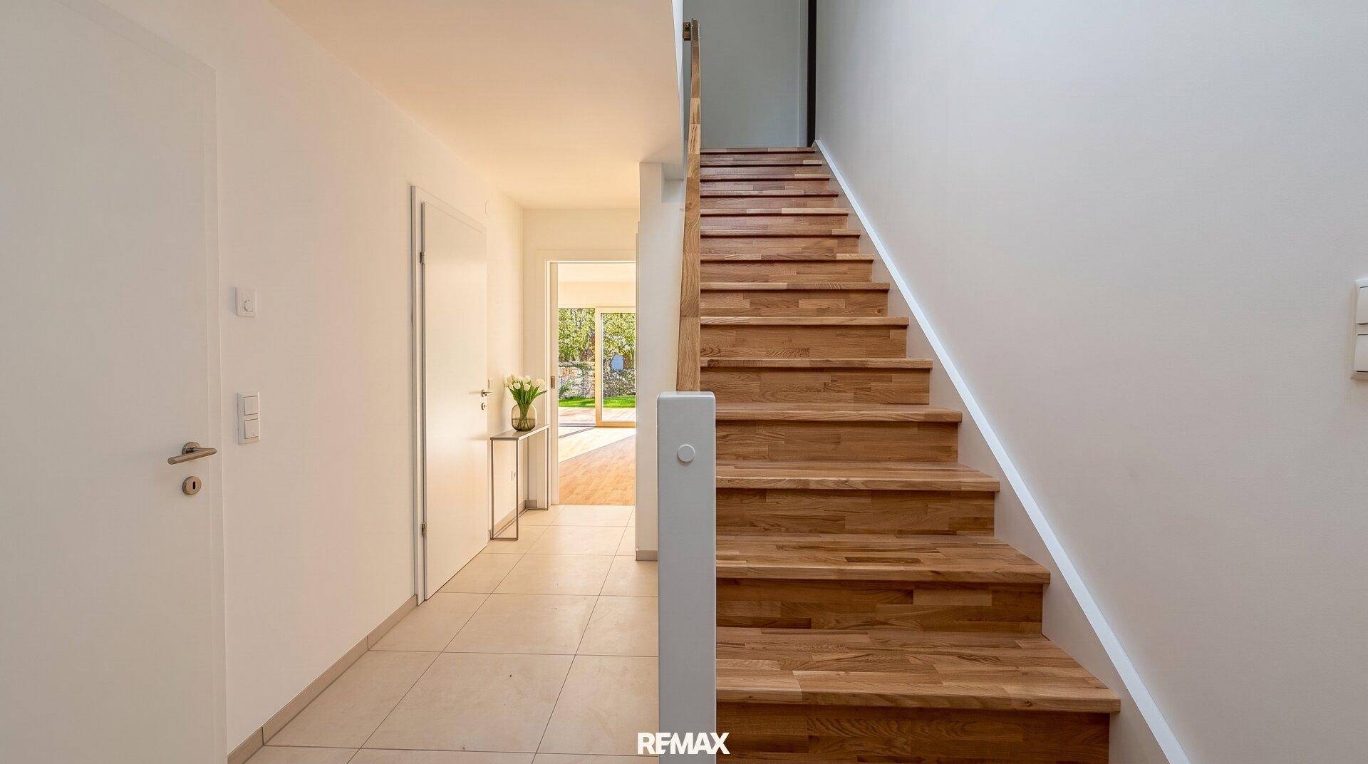Geräumiger Flur mit eleganter Holztreppe und hellem Fliesenboden.