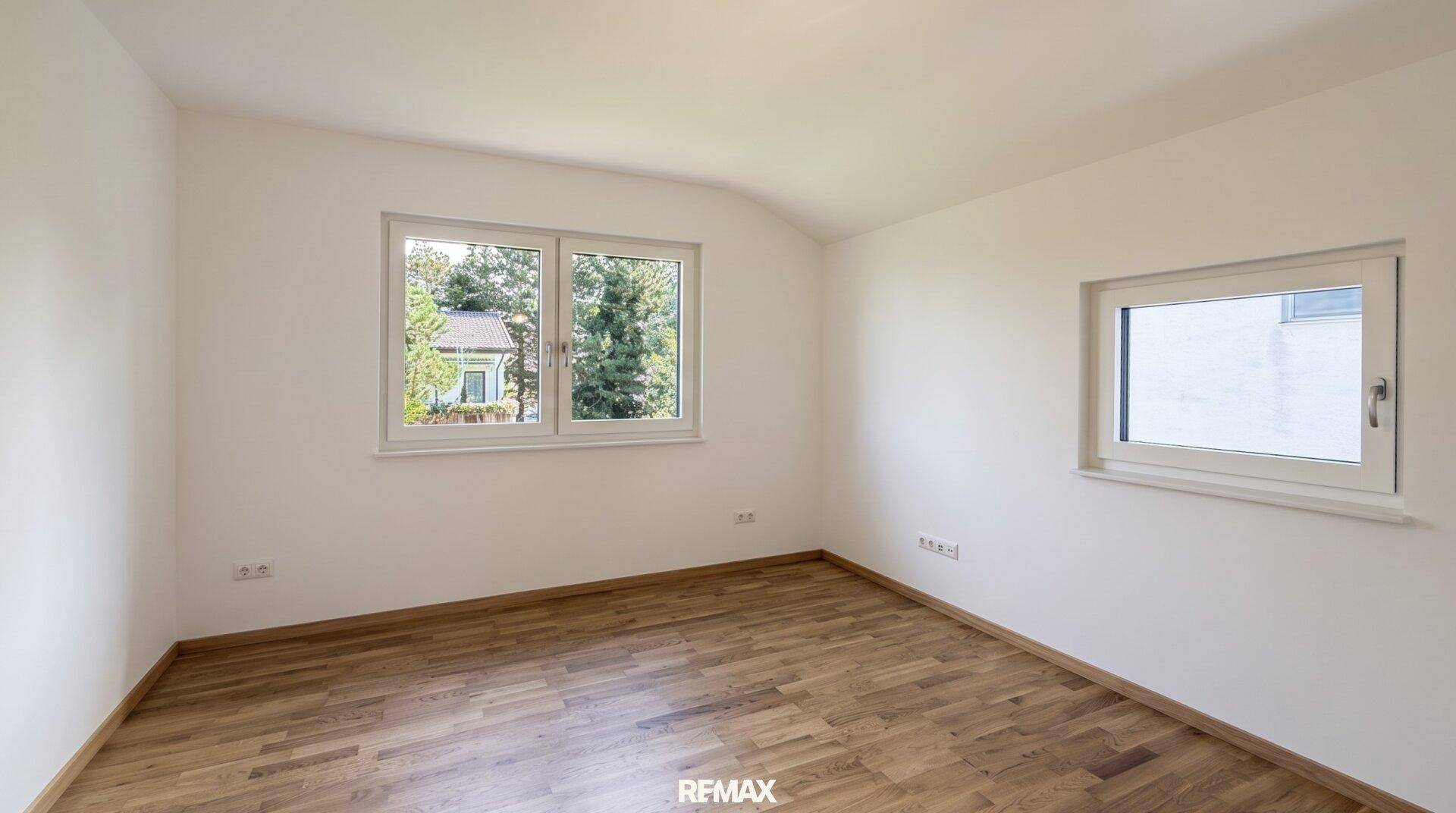 Geräumiges Schlafzimmer mit Holzboden und zwei Fenstern, die viel Licht hereinlassen.