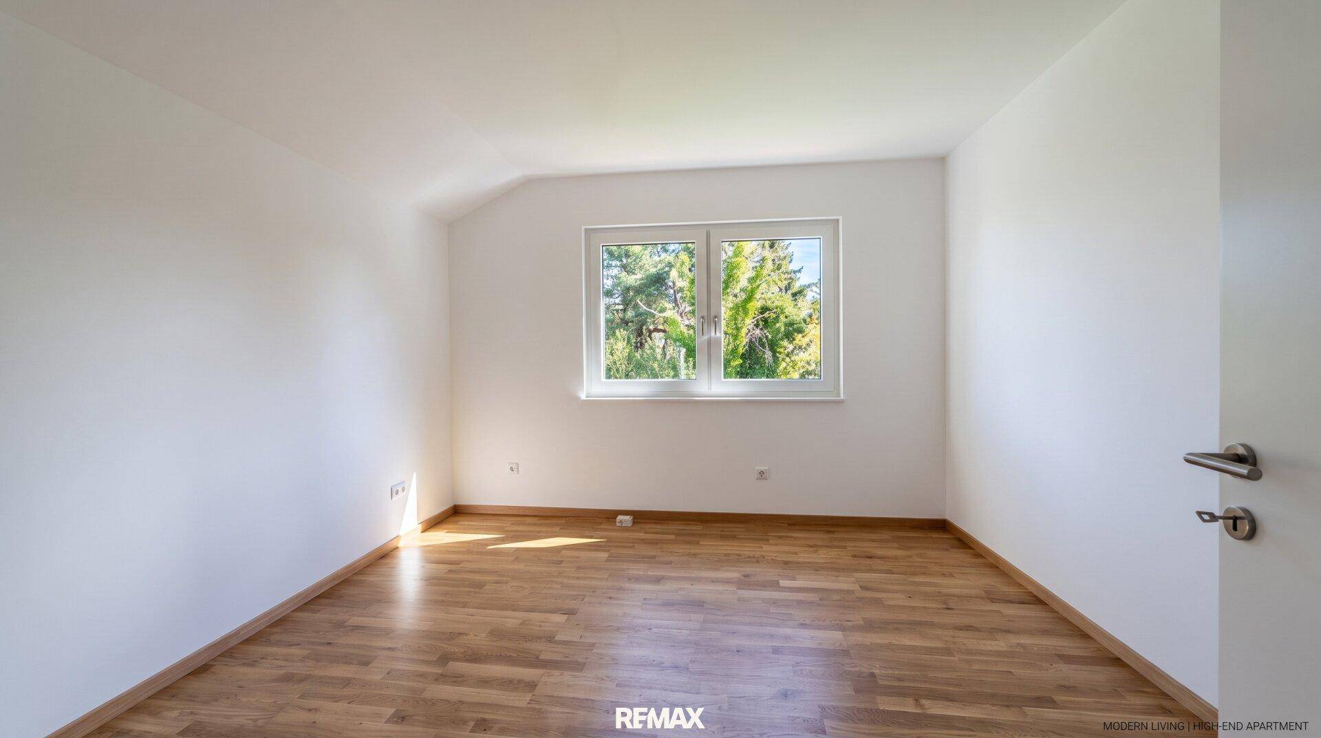 Helles Schlafzimmer mit Holzboden und großem Fenster mit Blick ins Grüne.