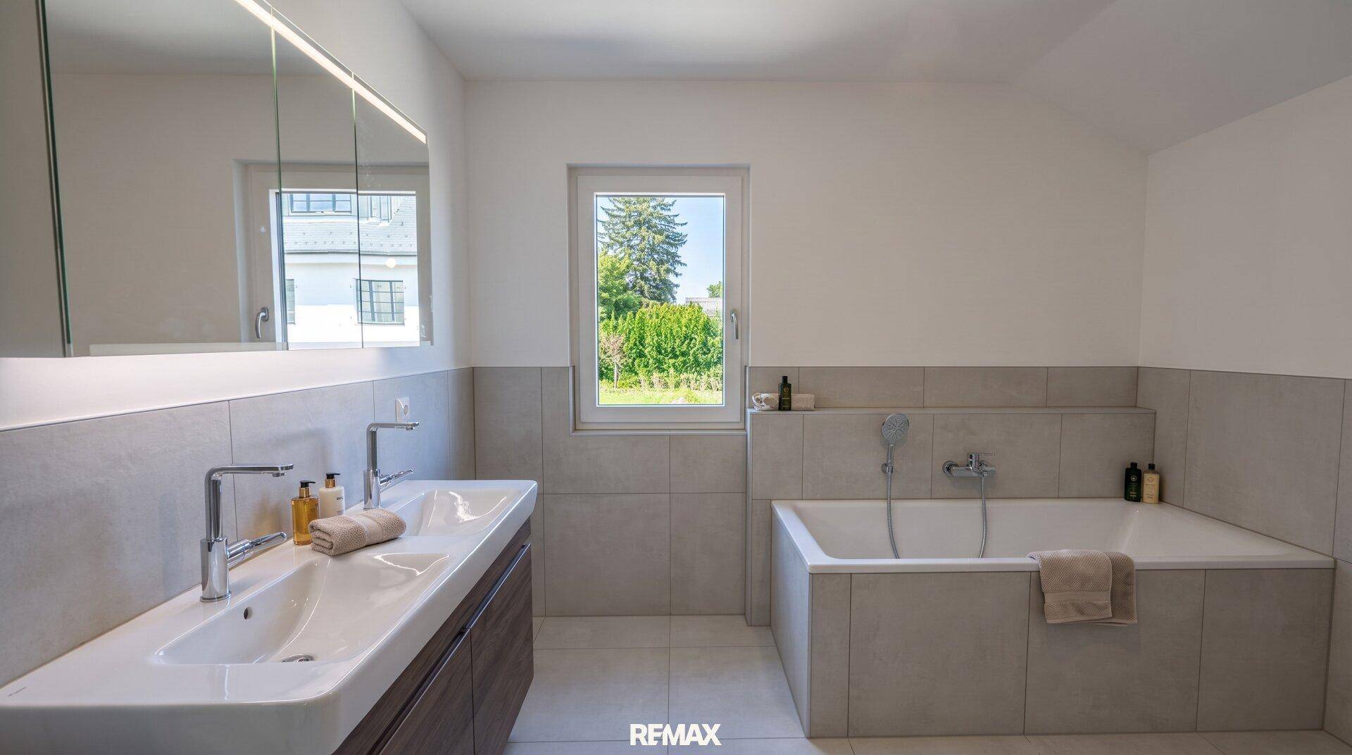 Modernes Badezimmer mit Doppelwaschbecken, Badewanne und Fenster mit Blick ins Grüne.