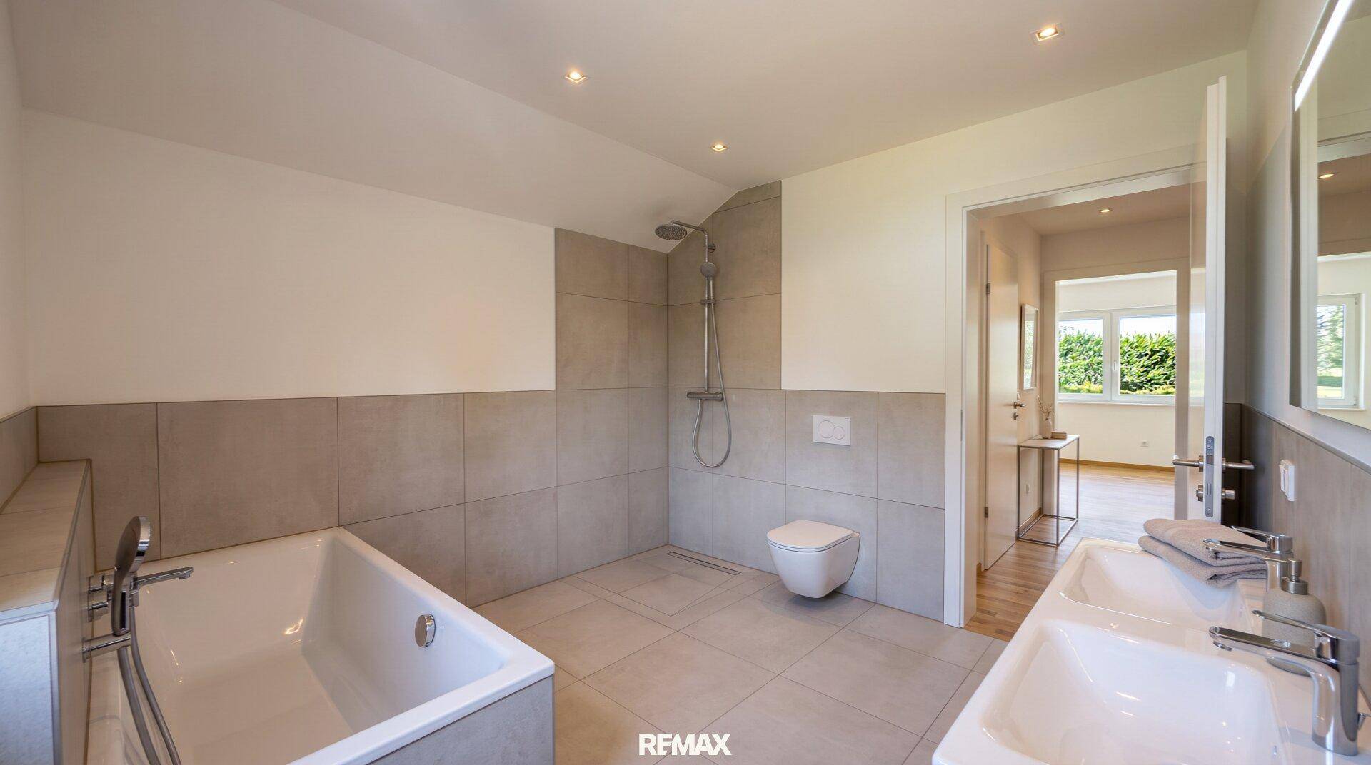 Helles Badezimmer mit Badewanne, bodengleicher Dusche und wandhängendem WC.