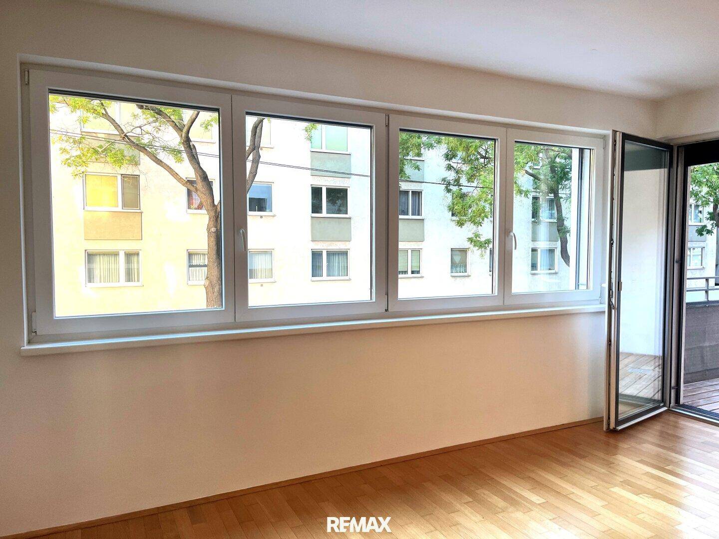 Heller Wohnraum mit großen Fenstern, Holzboden und Zugang zu einem Außenbereich.