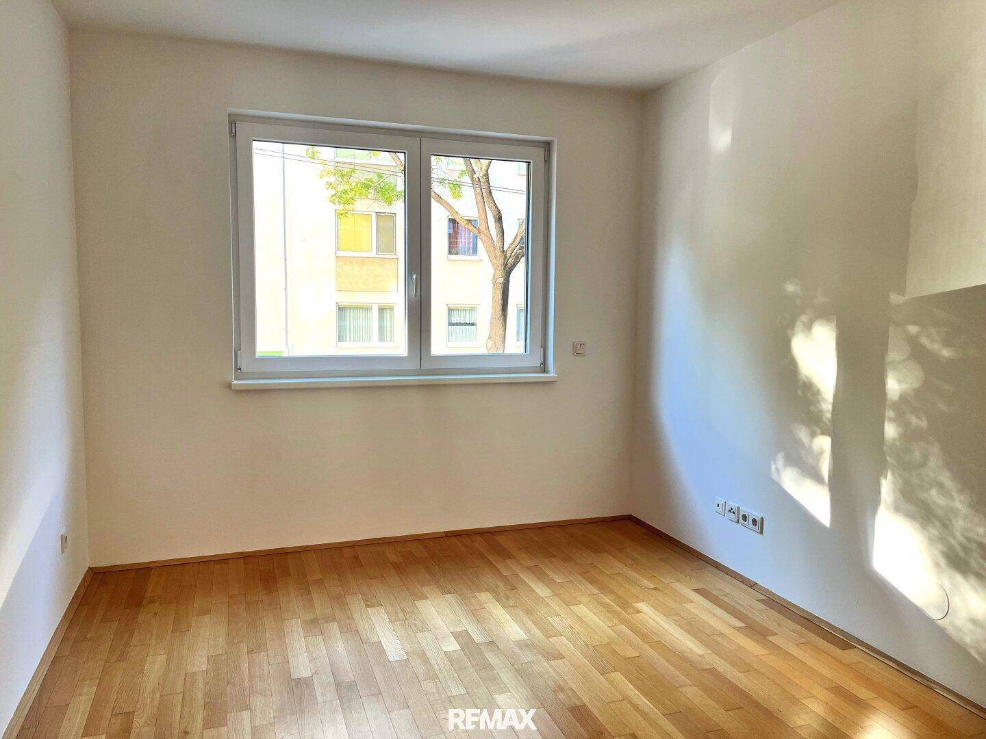Leeres Schlafzimmer mit Holzboden und einem Fenster mit Blick auf die Umgebung.