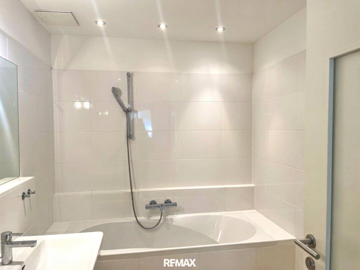 Helles Badezimmer mit weiß gefliesten Wänden, Badewanne und integrierter Dusche.