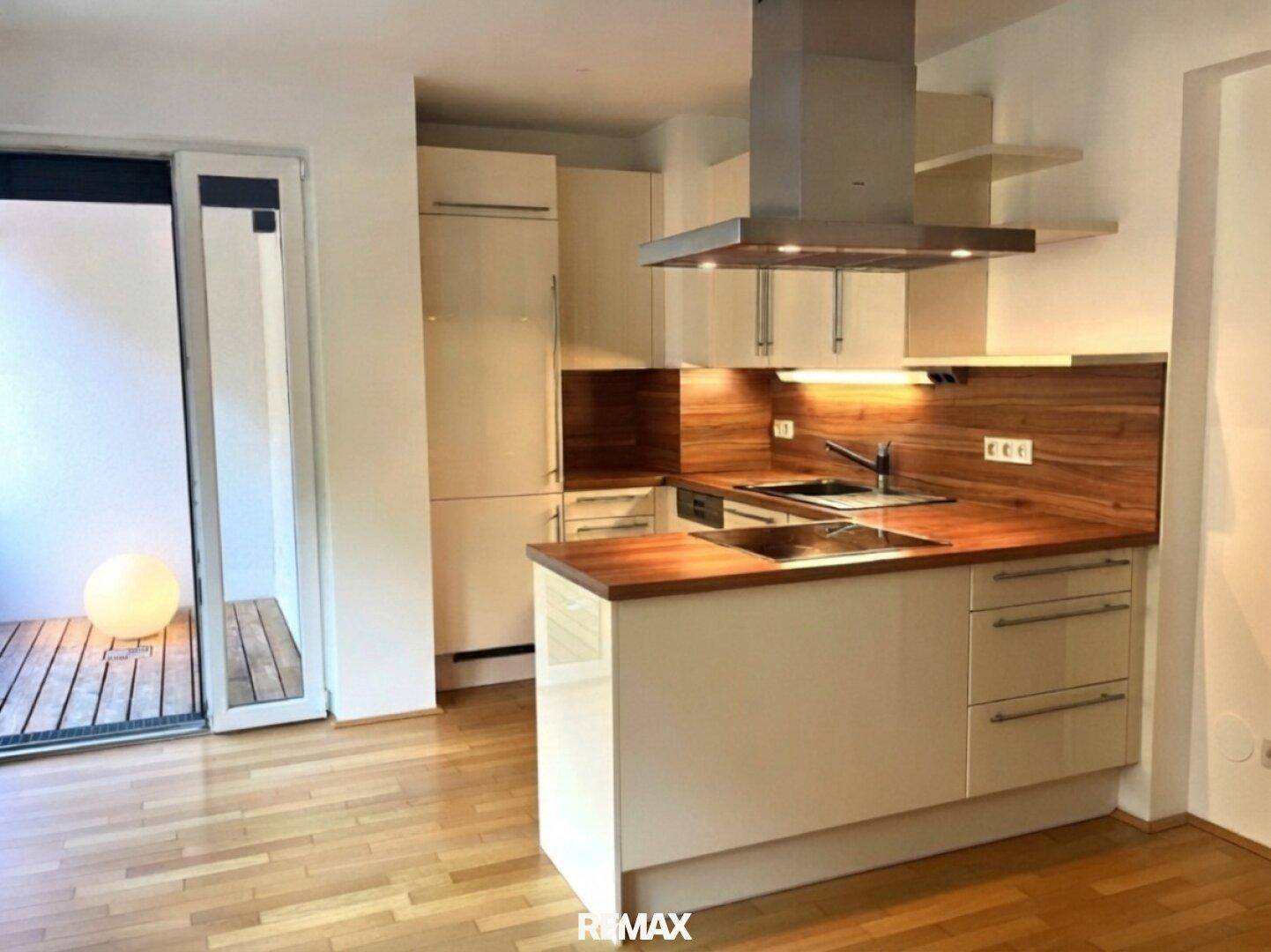 Moderne Einbauküche mit Holz-Arbeitsplatten, Kochinsel und Zugang zum Balkon.