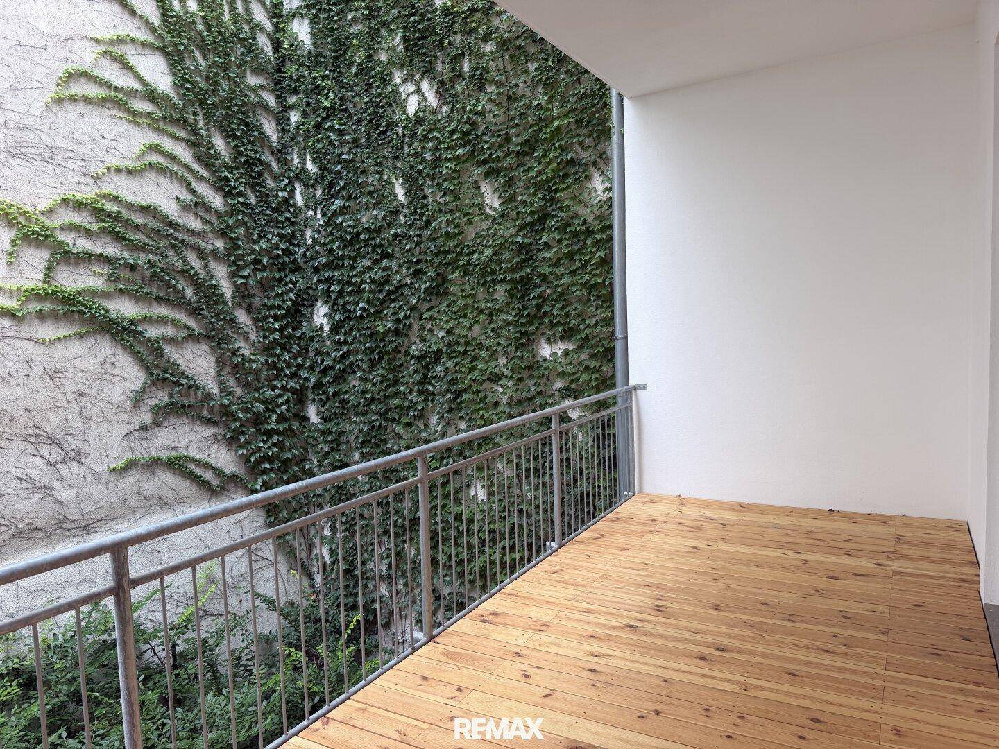 Geräumiger Balkon mit Holzbelag und einer von Efeu bewachsenen Wand, die eine natürliche Atmosphäre schafft.
