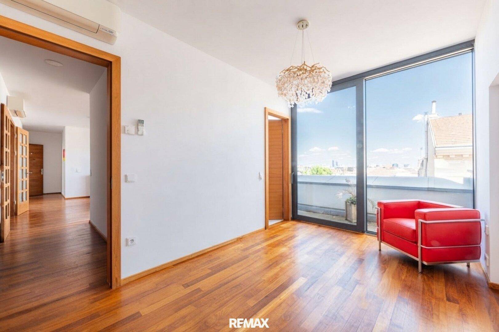 Heller Raum mit Holzboden, großen Fenstern und Zugang zu einem französischen Balkon.