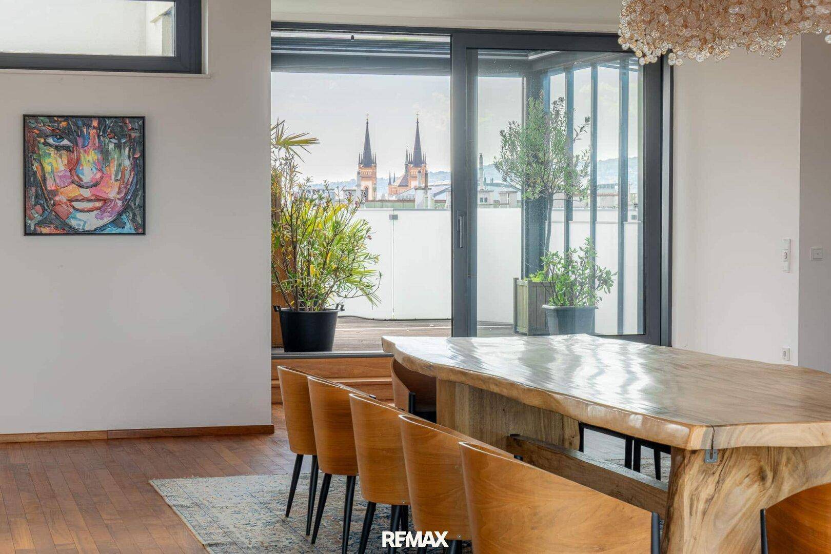 Essbereich mit Holztisch, modernen Stühlen und Blick auf die Stadt durch große Fenster.