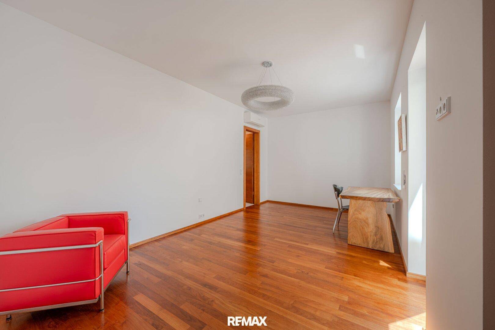 Heller, leerer Raum mit Holzboden, einem Schreibtisch und großen Fenstern.