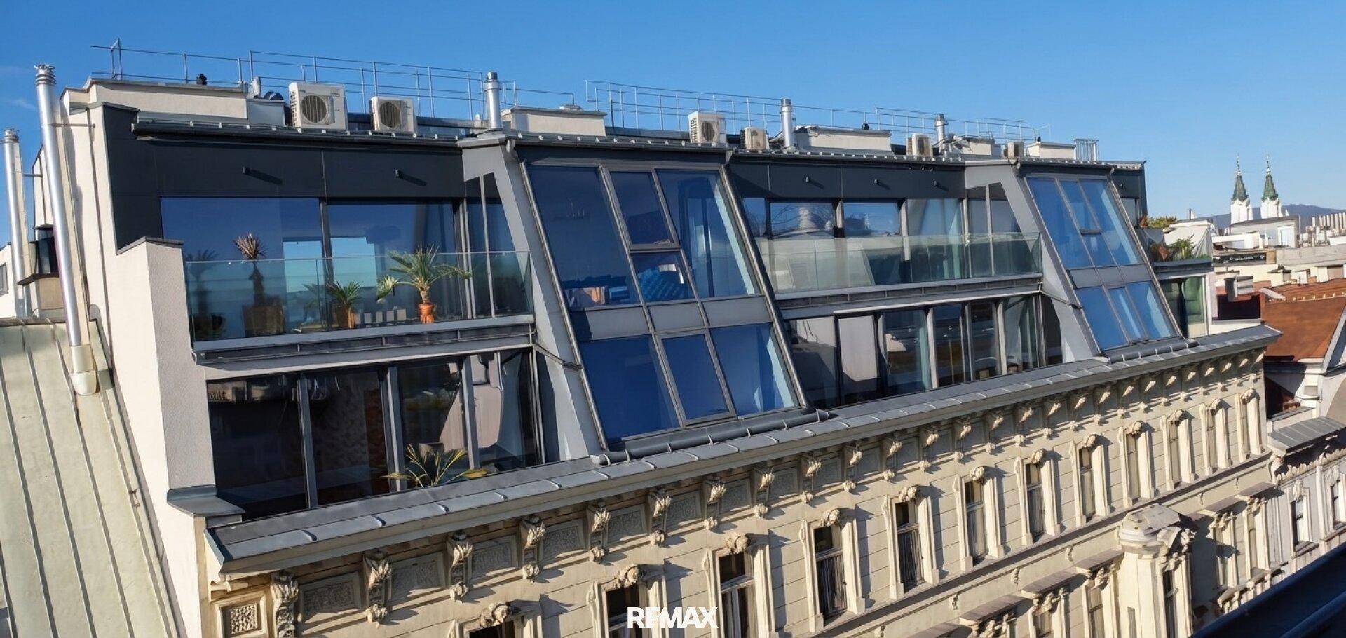 Moderne Dachgeschosswohnung mit großen Glasfronten und Terrassen in einem historischen Gebäude.