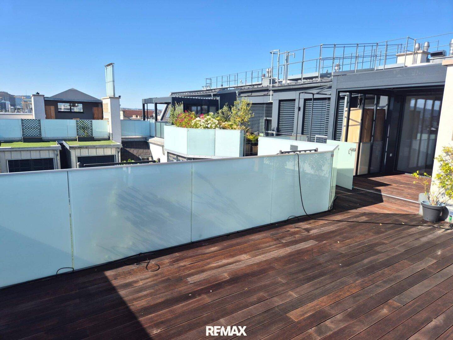 Weitläufige Dachterrasse mit Holzboden, Glasbrüstung und verschiedenen Pflanzen.