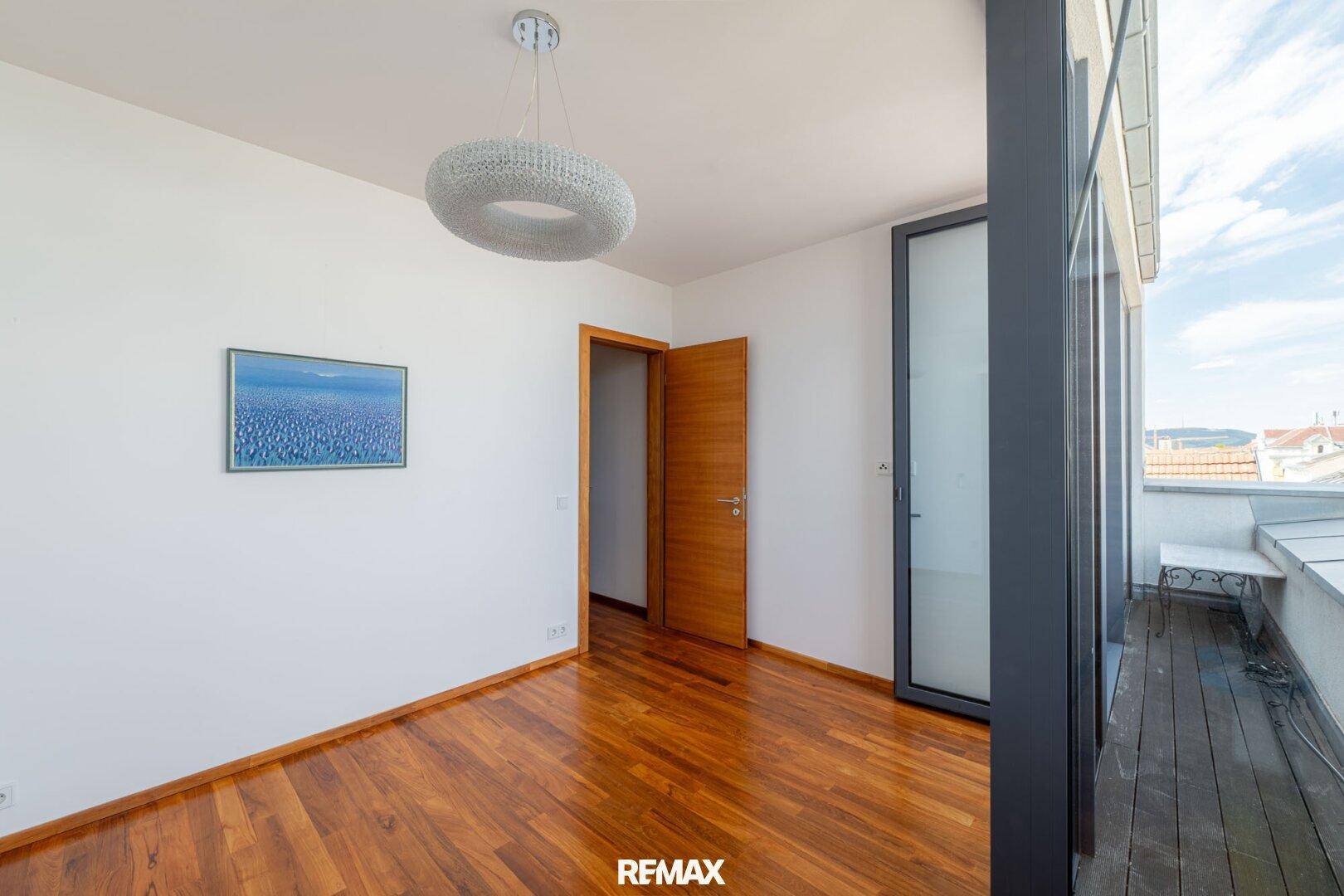 Helles Schlafzimmer mit Holzboden und Zugang zu einem kleinen Balkon.