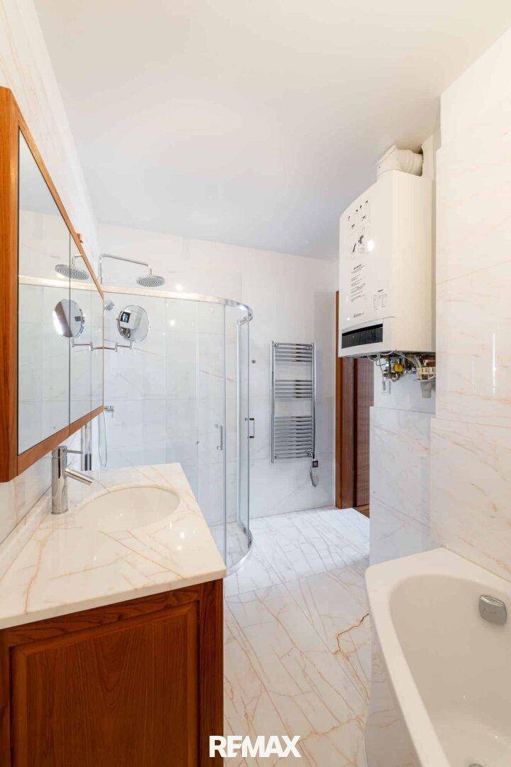 Modernes Badezimmer mit Badewanne, Dusche, Marmorwaschtisch und beheiztem Handtuchhalter.