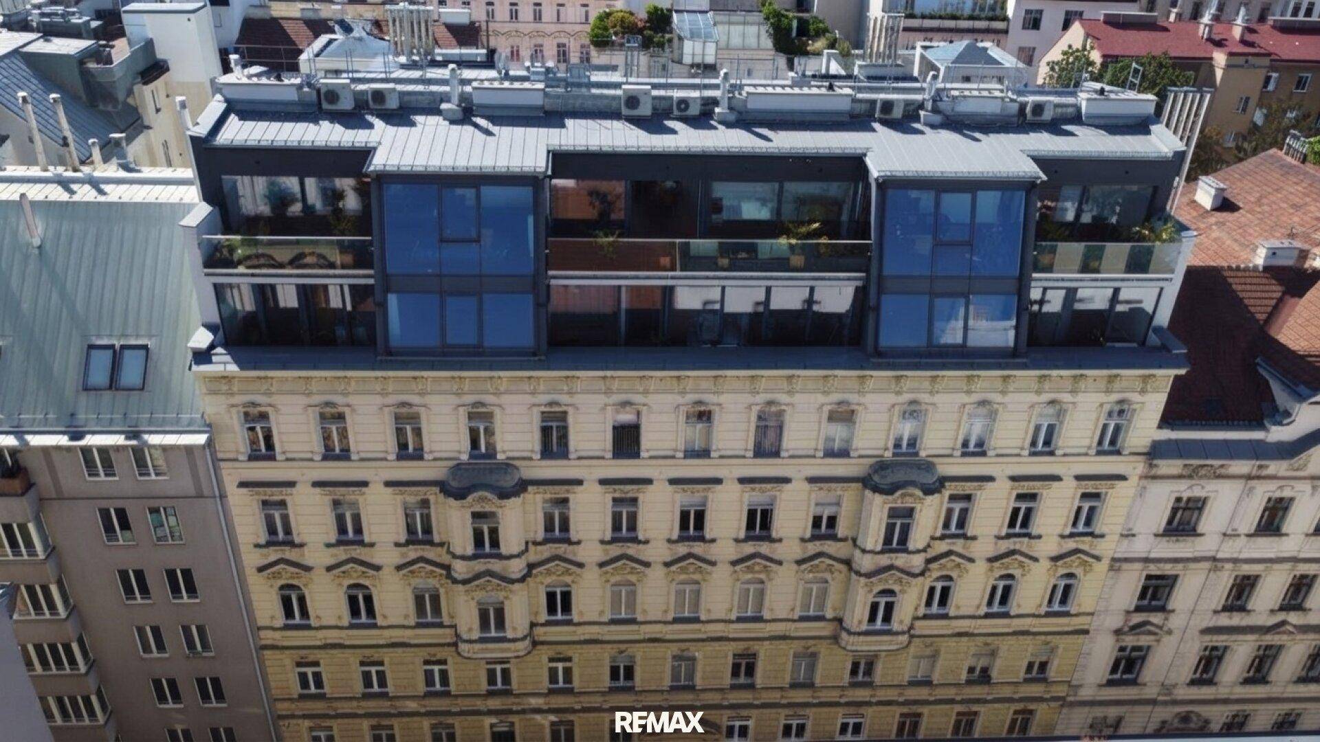 Luftaufnahme eines historischen Gebäudes mit modernem Dachausbau und Terrassen.