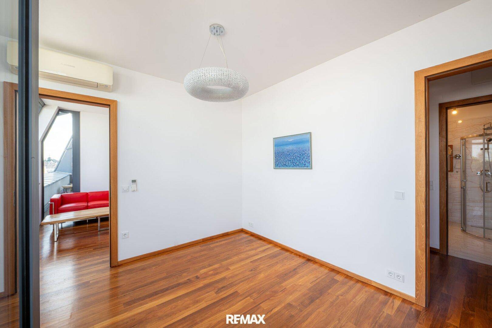 Schlafzimmer mit Holzboden, Klimaanlage und Zugang zu einem angrenzenden Raum.