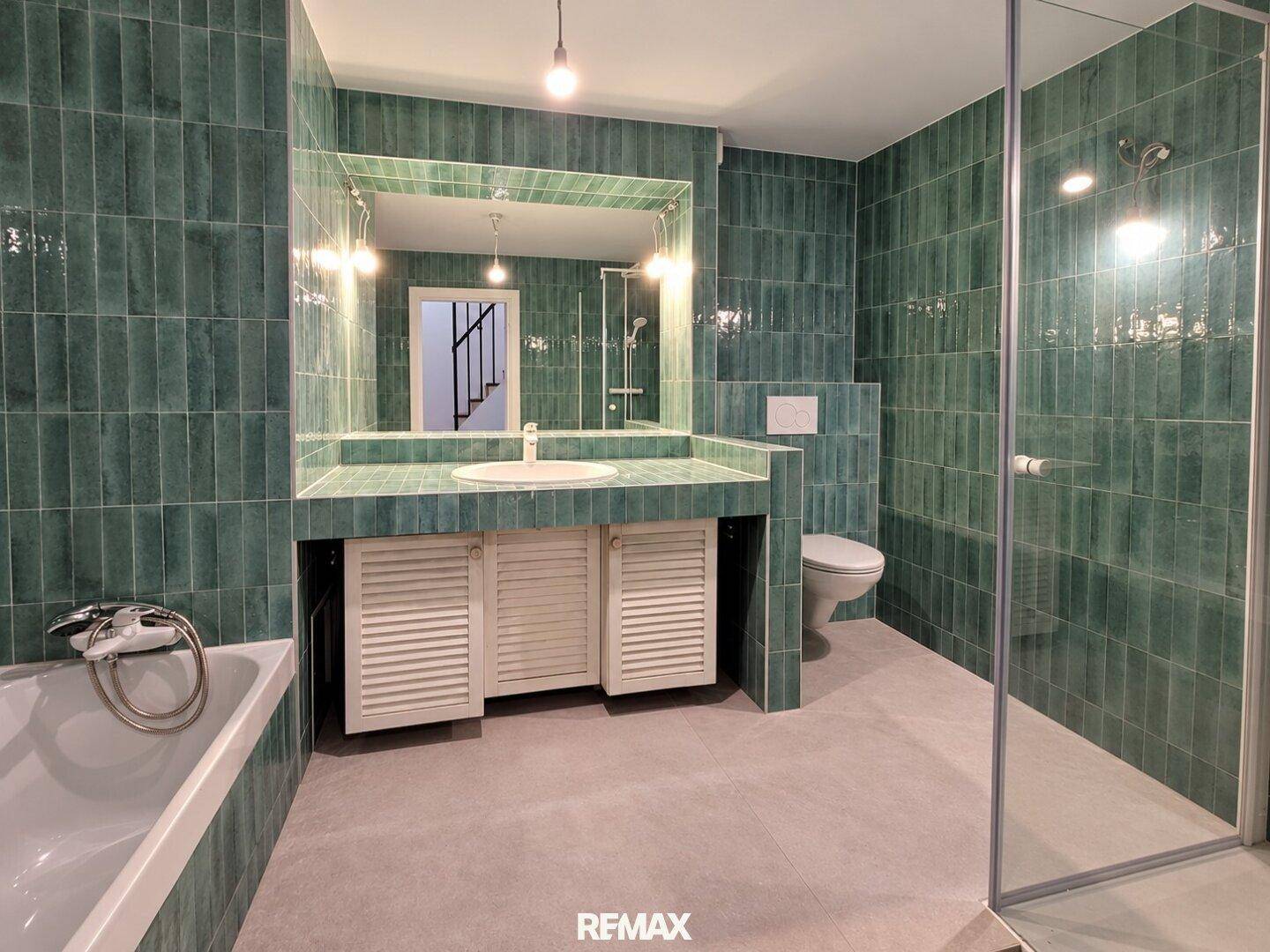 Modernes Badezimmer mit grünen Fliesen, Badewanne, Dusche und Einzelwaschbecken.