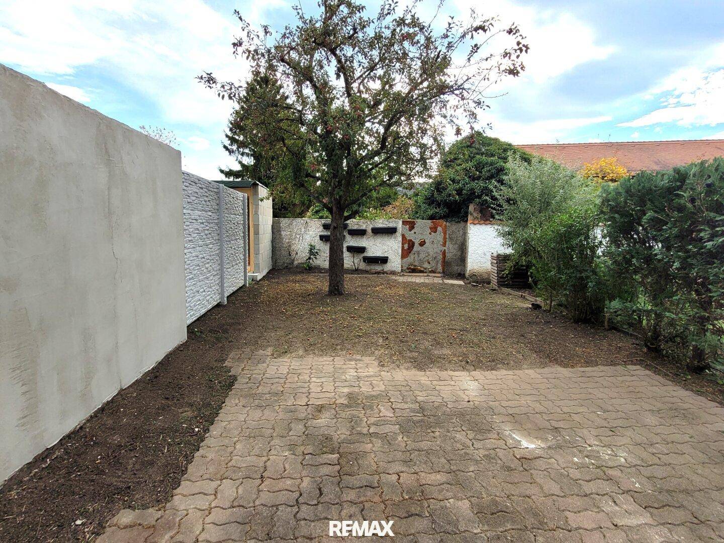 Kleiner, gepflasterter Gartenbereich mit einem Baum und einer Mauer, bereit zur Gestaltung.