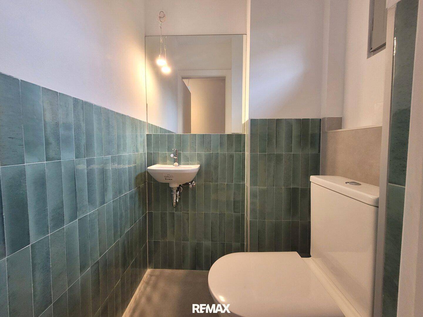Kleines Gäste-WC mit grünen Fliesen, Toilette und Einzelwaschbecken.