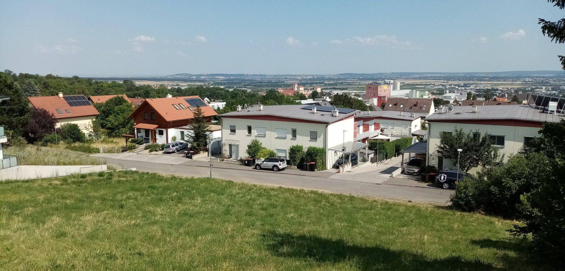 Panoramablick auf eine Wohnsiedlung und die weite Landschaft unter blauem Himmel.