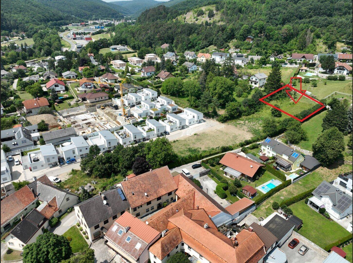 Weitläufige Luftaufnahme eines Baugebiets mit neuen Häusern und einem markierten Grundstück in hügeliger Landschaft.