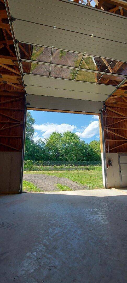 Blick aus der Lagerhalle durch das geöffnete Rolltor auf grüne Landschaft und Bäume.