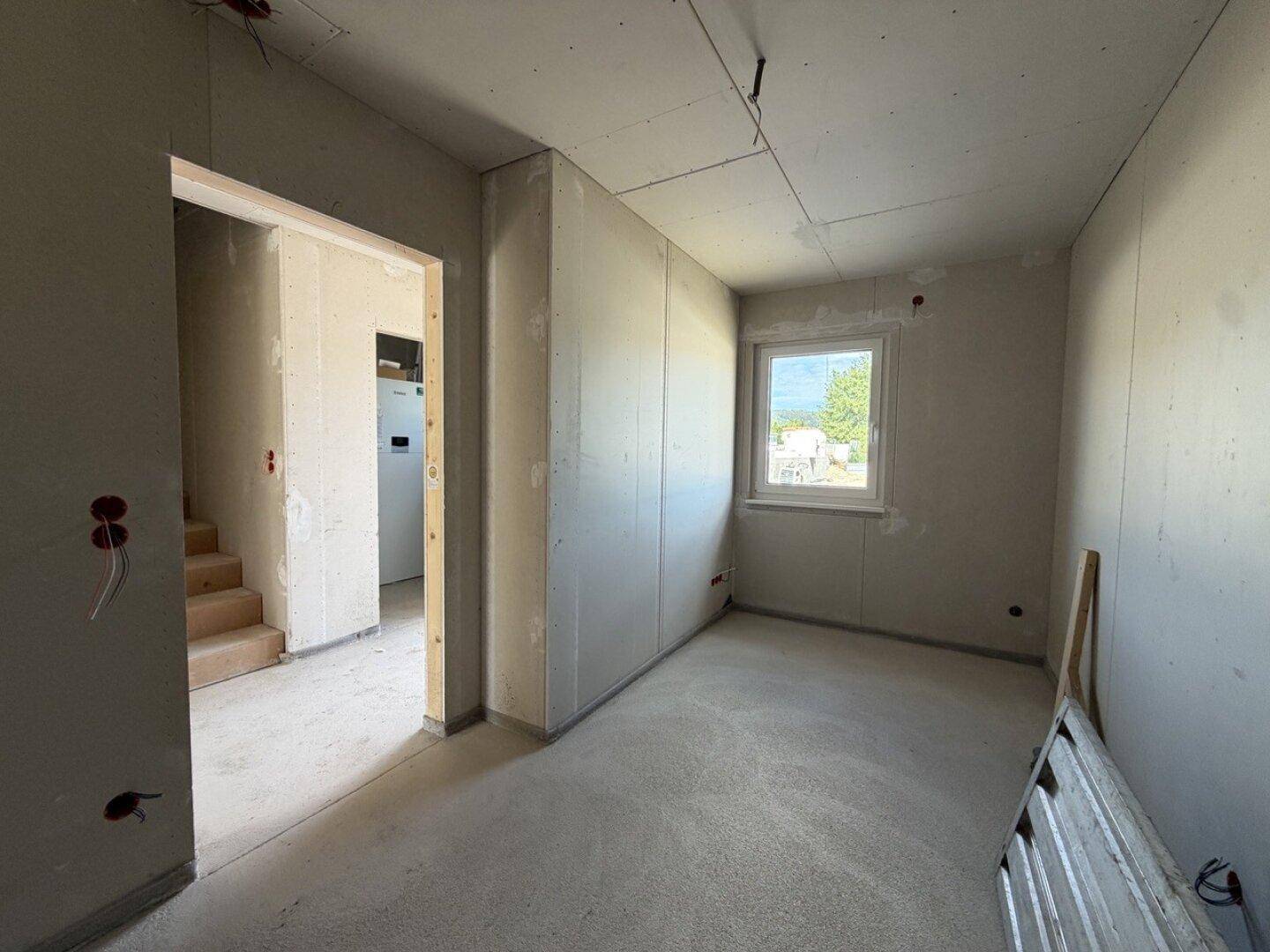 Zimmer im Rohbau mit Fenster und Zugang zum Treppenhaus, viel Potenzial.