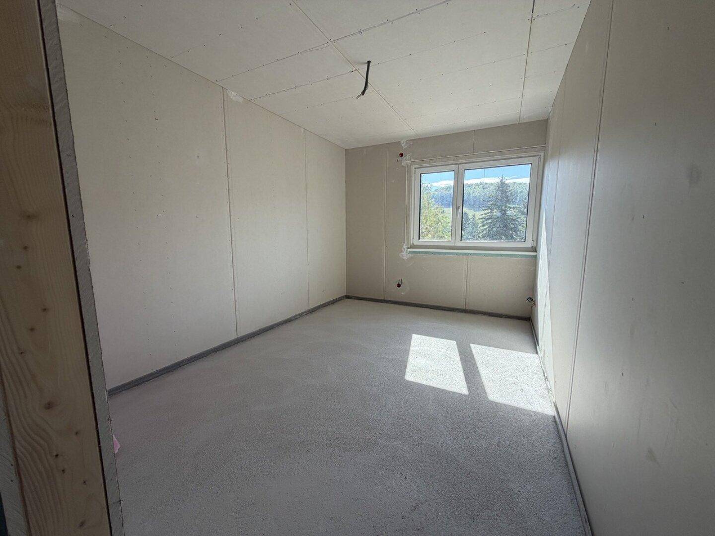 Weiteres Zimmer im Rohbau mit Fenster und sonnigem Lichteinfall.