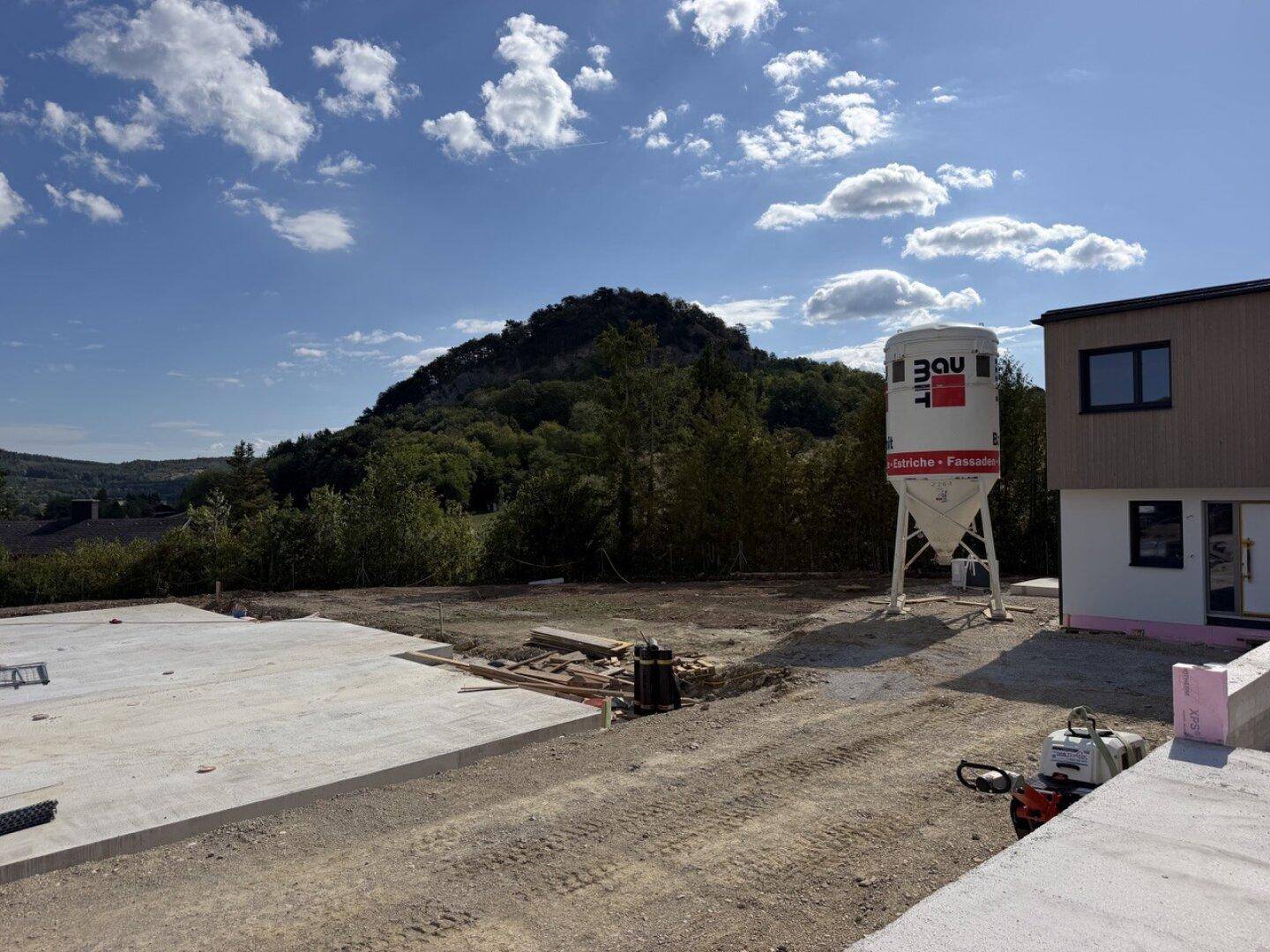Baustelle mit Blick auf die umliegende Hügellandschaft und einen Zementsilo.