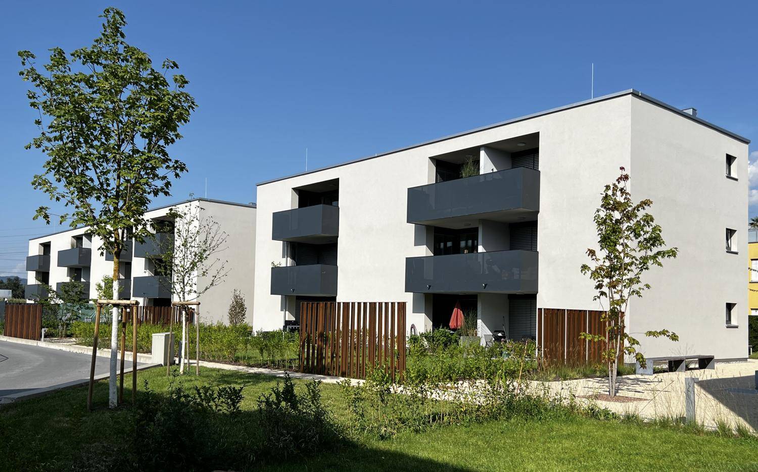 Moderne Wohngebäude mit Balkonen und gepflegten Grünflächen unter blauem Himmel.
