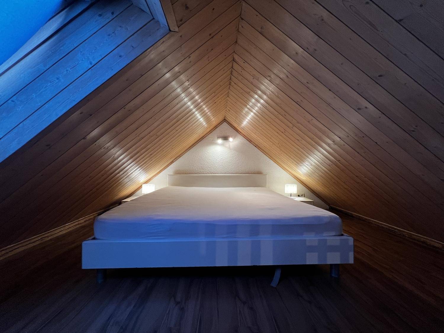 Gemütliches Schlafzimmer im Dachgeschoss mit Holztäfelung und indirekter Beleuchtung.