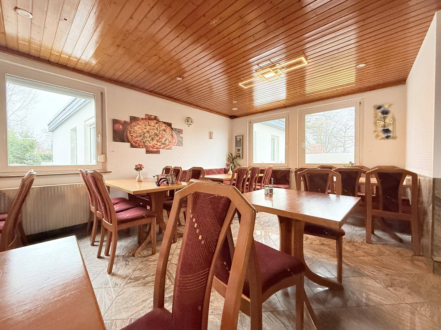 Heller Essbereich mit Holztäfelung an der Decke und mehreren Tischen und Stühlen.