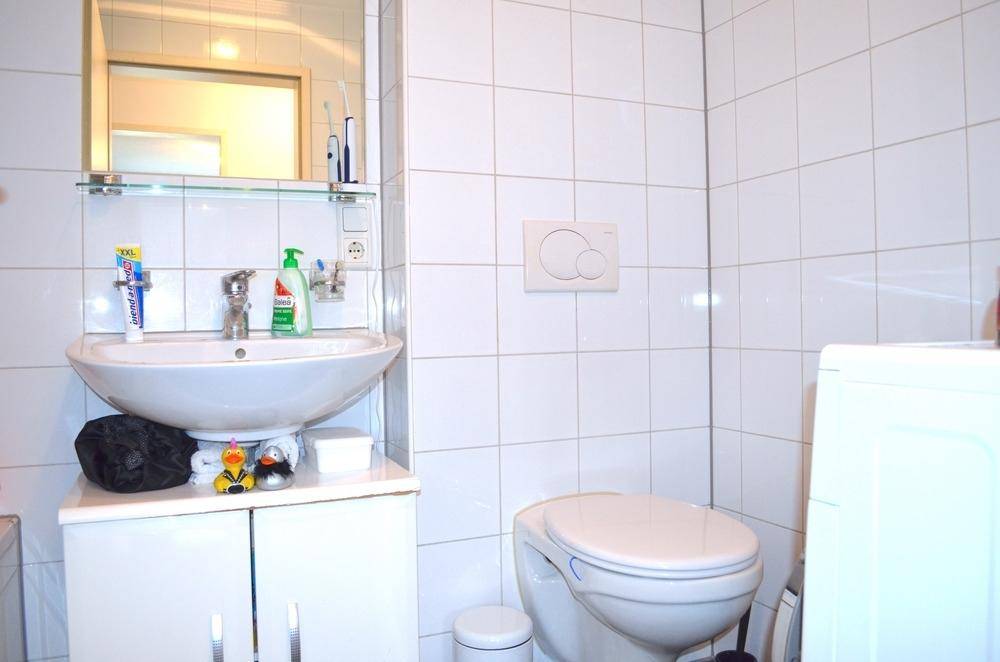Modernes Badezimmer mit weißen Fliesen, Waschbecken mit Unterschrank und wandhängendem WC.