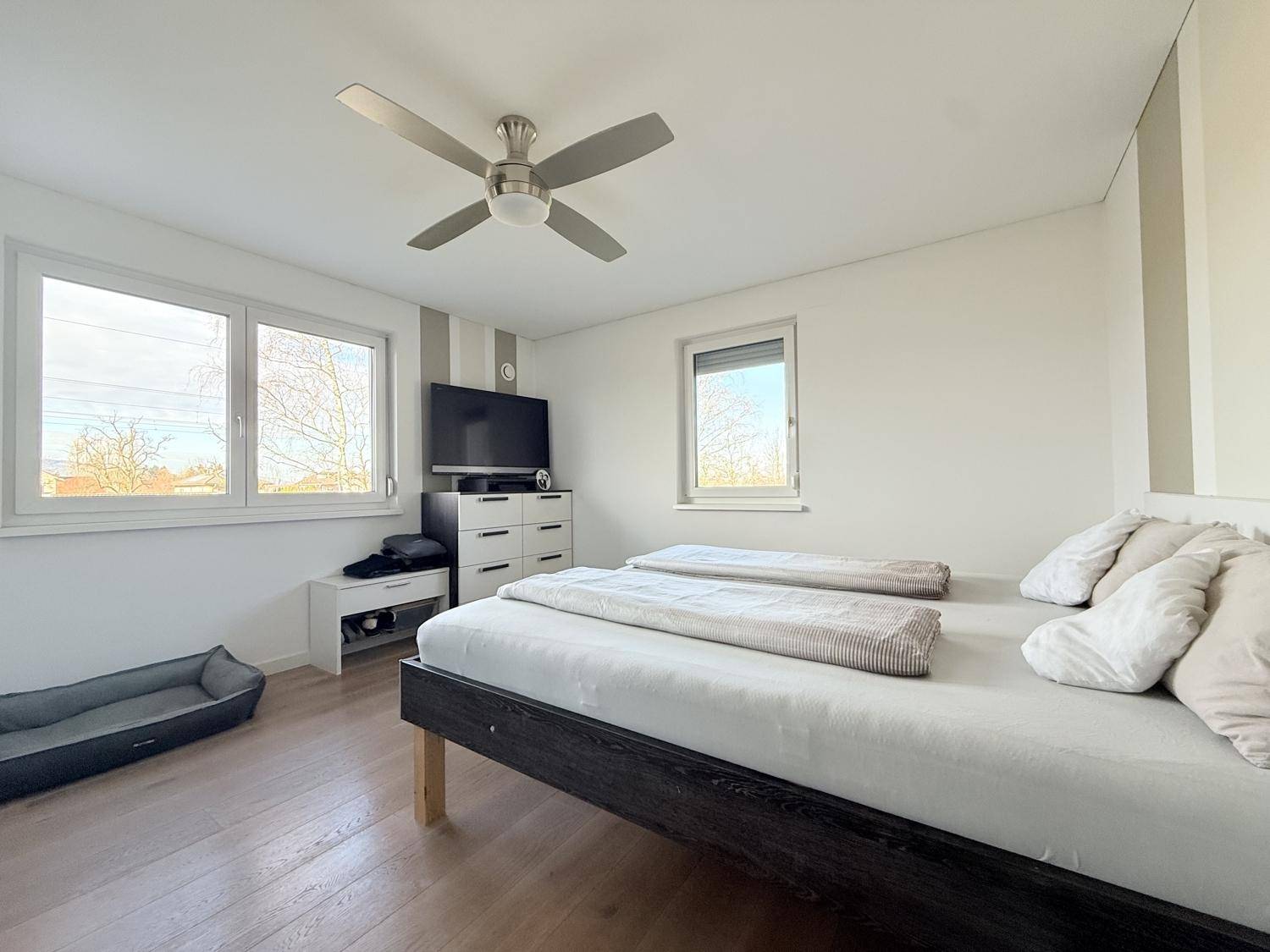 Schlafzimmer mit Doppelbett, Fernseher und großen Fenstern für viel Tageslicht.