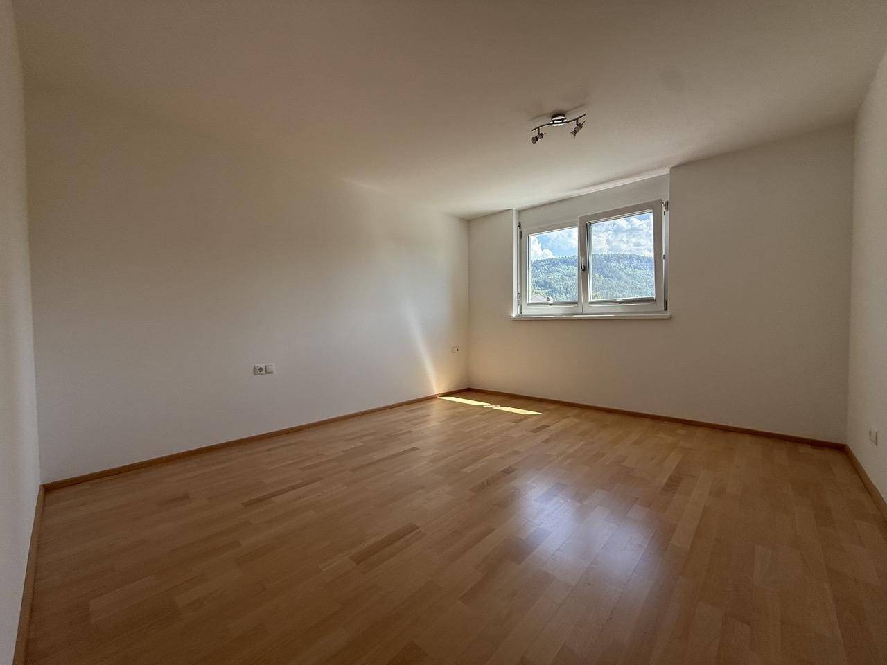 Helles Schlafzimmer mit Holzfußboden und Blick auf die grüne Umgebung.